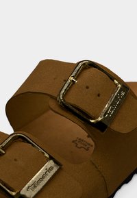 Sandales en cuir marron avec deux brides réglables, boucles dorées et surface texturée. Logo visible sur la semelle intérieure.