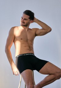 Zwarte boxershorts met een zachte tailleband met de tekst "DANISH ENDURANCE" in witte letters, gedragen door een model dat op een kruk zit.