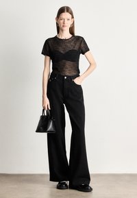 Top preto transparente riscado, jeans largos pretos de cintura alta e uma pequena bolsa preta. Apresenta sapatos planos de plataforma e brincos de argola simples.