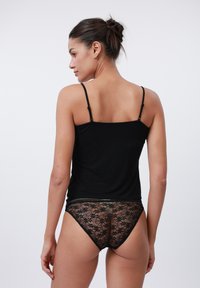 Camisolă neagră cu bretele subțiri, asortată cu chiloți negri din dantelă cu model floral și un elastic cu accente metalice.