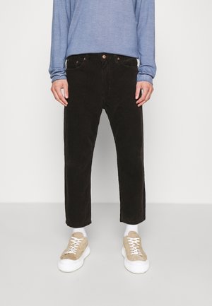 Braune Cordhosen im geraden Schnitt, mit Fünf-Taschen-Design und kontrastierenden sandfarbenen Sneakers mit weißen Sohlen. Pullover aus blauer Stoff.