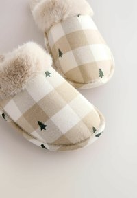 Beige and white checkered slippers with small green tree patterns and plush fur lining around the opening, placed on a light surface.