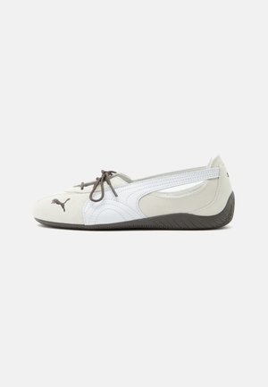 Weißer und grauer Slip-On-Sneaker mit braunen Schnürsenkeln, Puma-Logo vorne und strukturierter dunkler Sohle, seitlich auf weißem Hintergrund gezeigt.