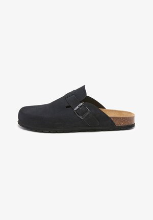 Sabot en suède noir avec une boucle argentée réglable, une semelle en liège et une semelle en caoutchouc texturée. Design à dos ouvert pour un enfilage facile.