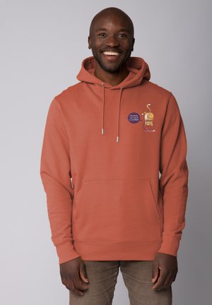 Orange Kapuzenpullover mit Kängurutasche, featuring ein Cartoon-Design und zwei bestickte Patches. Hergestellt aus weichem Stoff, mit Kordelzügen und gerippten Bündchen.