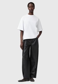 Witte oversized t-shirt met reliëftekst, gecombineerd met losse zwarte leren broek en platte zwarte schoenen met zilveren studs.