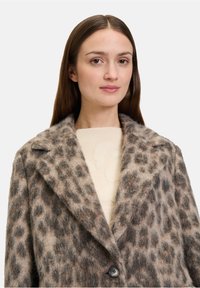 Płaszcz w zwierzęcy wzór w cętki, o miękkiej, puszystej fakturze, z klapami i pojedynczym czarnym guzikiem. Tło jest białe.
