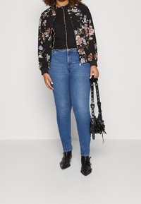 Svart blommig bomberjacka med färgglada blommönster, matchad med en svart topp, blå skinny jeans och svarta ankelstövlar. Håller på en svart väska.