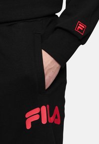 Zwarte katoenen joggers met een zijzak; voorzien van een gedurfde rode "FILA" logo en een rode geborduurde logo op de mouw voor contrast en branding.
