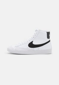 Høye sneakers i hvitt skinn med en svart suedebånd fra Nike og en svart bakpanel. Har hvite snøringer og en teksturert gummisåle.
