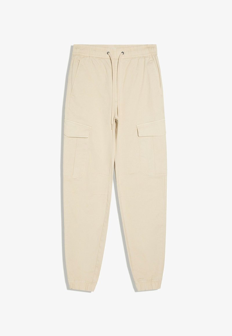 Pantalon cargo beige avec taille élastique, cordon de serrage, deux poches latérales, deux grandes poches à rabat sur les jambes et poignets élastiques.