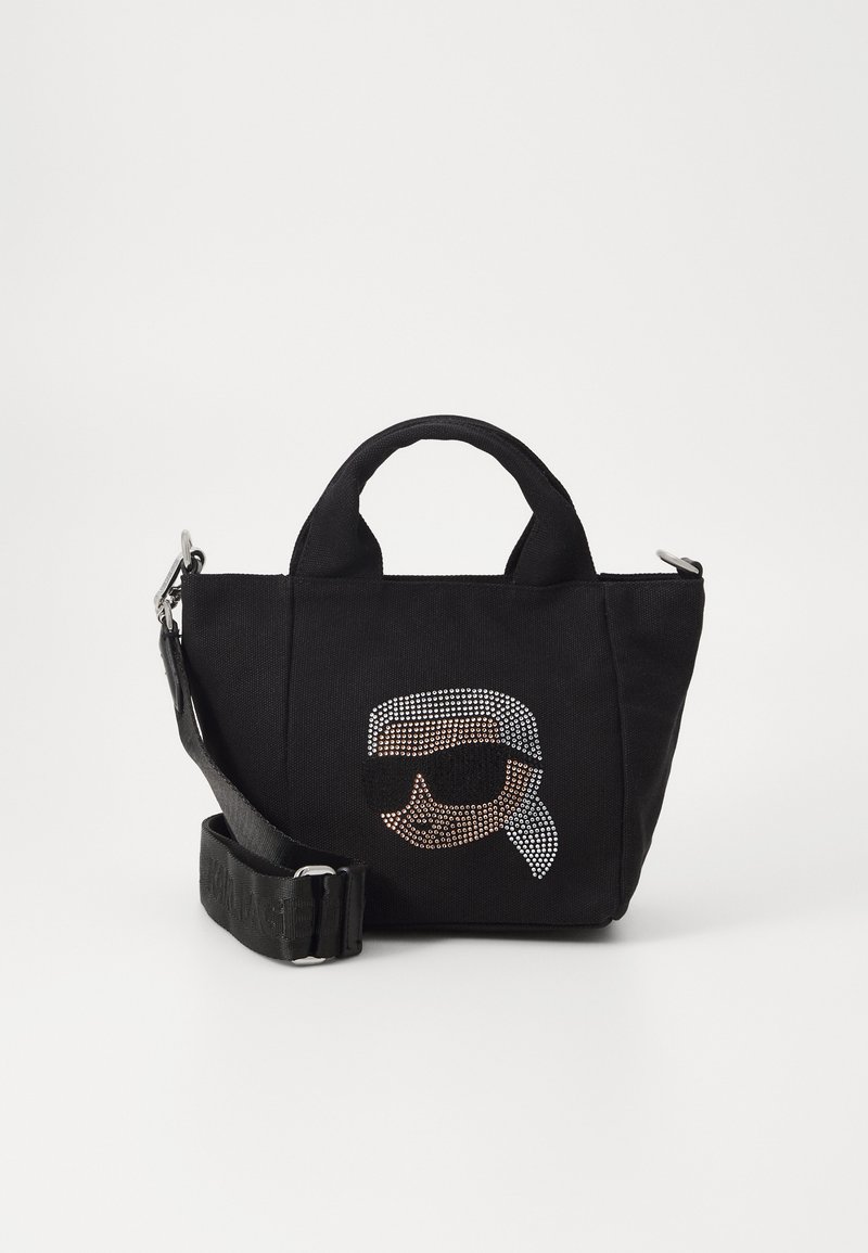 Black canvas handbag with crystal embellishment depicting a face in sunglasses. Features dual handles and an adjustable shoulder strap.