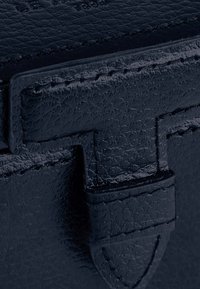 Borsa in pelle di un blu scuro, caratterizzata da una finitura testurizzata, dettagli cuciti e una chiusura con tracolla piatta. I dettagli includono un bordo liscio e un logo impresso.