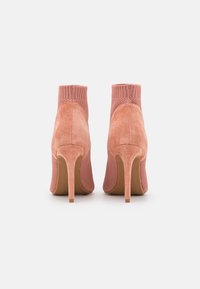 Stivaletti con tacco rosa che presentano una tomaia in maglia texturizzata e un tacco in suede liscio. Il design include una punta affusolata e un tacco a stiletto sottile.
