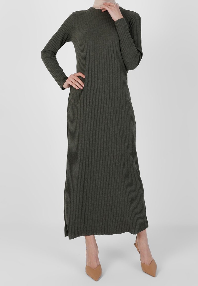 Robe longue côtelée vert olive foncé avec manches longues et fentes latérales, en tissu texturé. Associée à des talons pointus beiges.