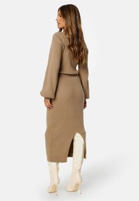 Abito a maglia, a maniche lunghe, a coste in beige con vita aderente, spacco laterale e lunghezza a metà polpaccio, abbinato a stivali col tacco a spillo color crema.