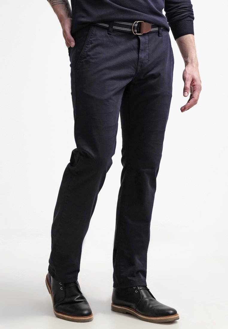 Marineblauwe chino's van katoen, met een slim fit, zijzakken en een bruine leren riem met een zilveren gesp. Gemaakt in combinatie met zwarte leren schoenen.
