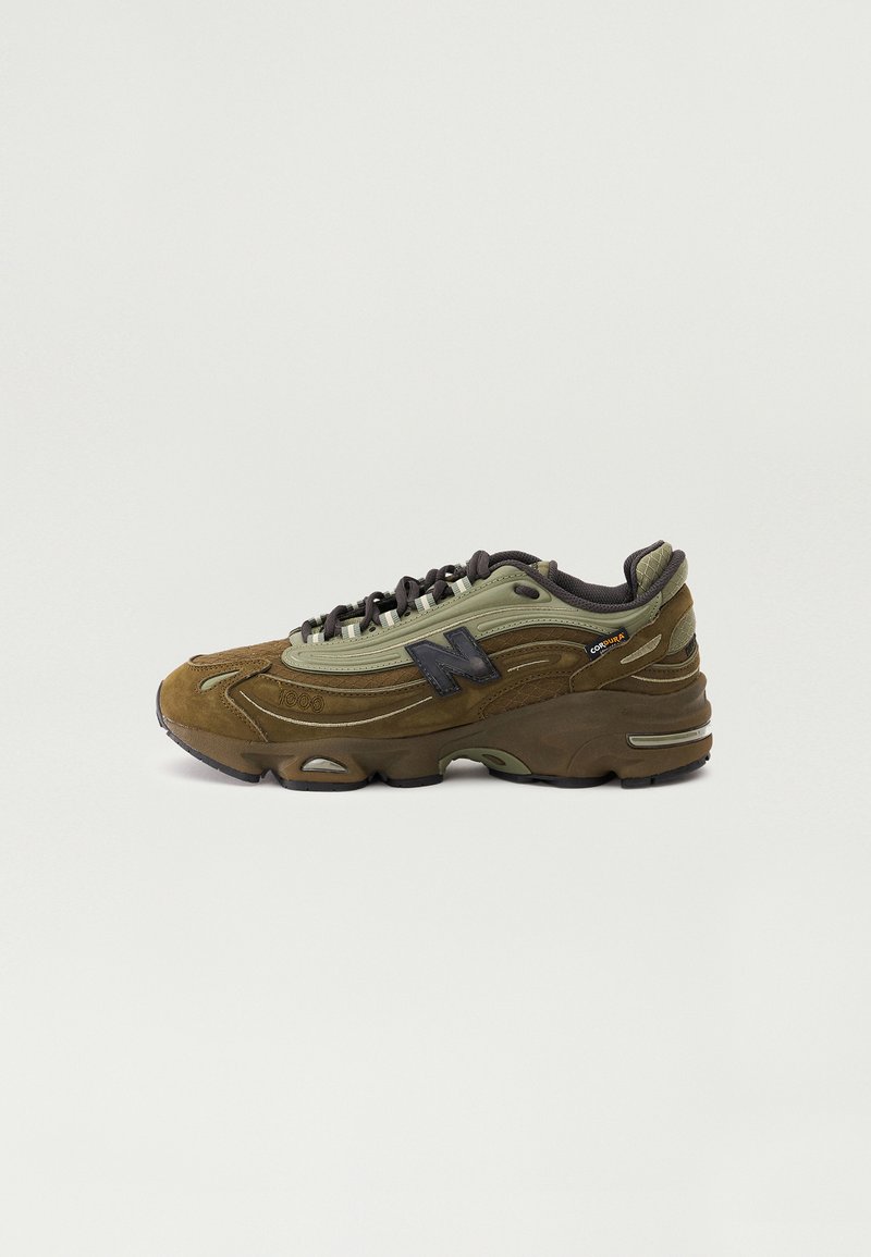 Scarpe sportive marroni e verde oliva con materiali in camoscio e rete, suola in gomma, design con lacci e dettaglio di marchio visibile sul lato.