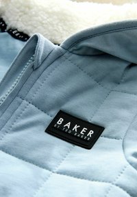 Jasnoniebieska pikowana tkanina z miękką podszewką, z czarną prostokątną metką z napisem "BAKER by TED BAKER". Zamek błyskawiczny.