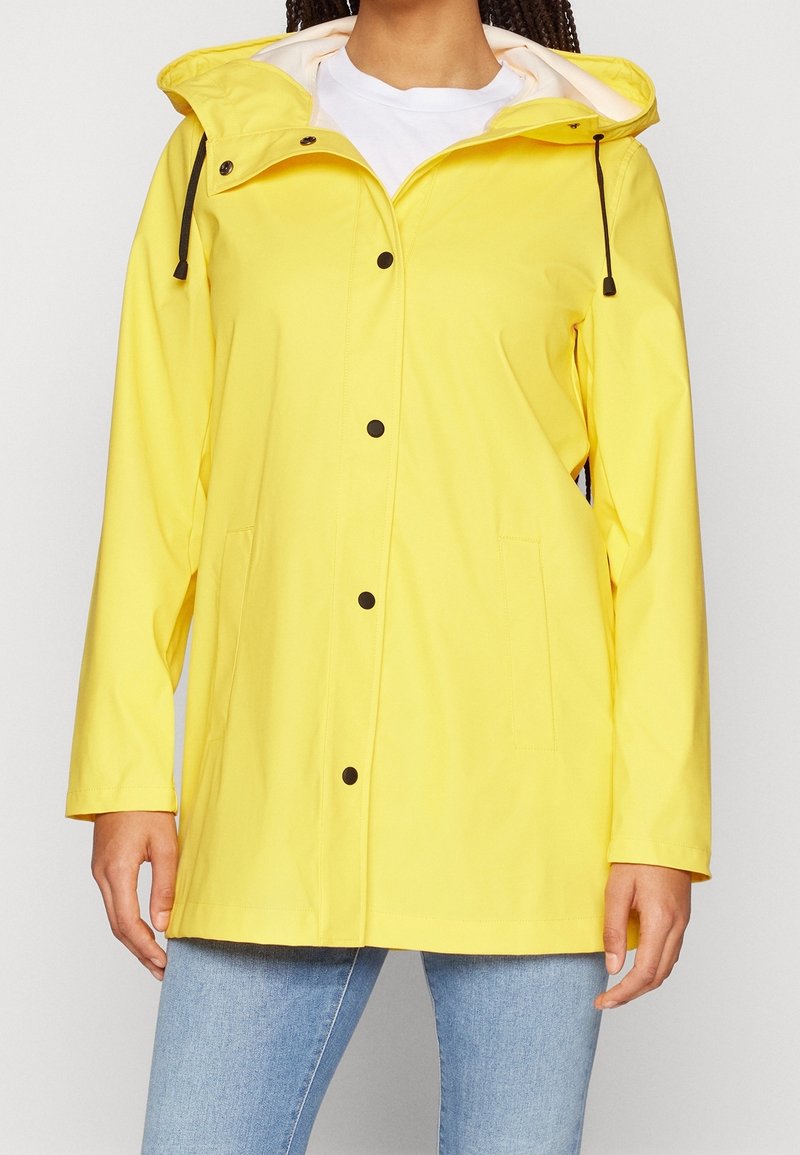 Veste de pluie imperméable jaune avec capuche, boutons-pression et deux poches latérales ; texture de tissu lisse ; accents de quincaillerie noirs contrastants.