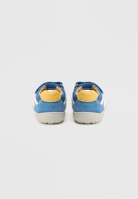 Pantofi din piele intoarsa albastra cu accente galbene pe toc si talpi de cauciuc gri. Au o curea cu velcro pentru inchidere si elemente albe de design pe laterale.