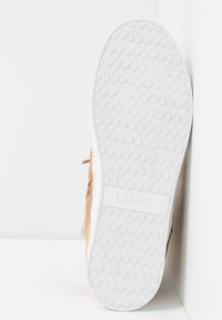 Suola di sneaker in gomma bianca, con un motivo testurizzato per la presa. Parte superiore in suede marrone chiaro con una cerniera laterale e logo del marchio.