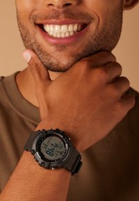 Montre digitale avec un bracelet en caoutchouc noir et un cadran rond affichant l'heure en grands chiffres. Présente des boutons et un design robuste.
