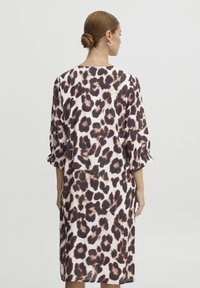 Robe à imprimé léopard avec des manches trois-quarts, en tissu lisse, présentant des taches brunes sur un fond clair, longueur genou.