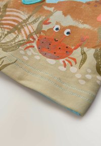 Detská košeľa z ľahkej béžovej látky s potlačou kraba v oranžovej, hnedej a červenej farbe, obklopená zelenými morskými riasami a bielymi bublinami.