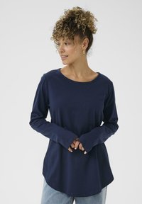 Maglietta a maniche lunghe color blu navy realizzata in un tessuto morbido, con un collo arrotondato e una vestibilità comoda. Presenta polsini leggermente svasati e un orlo curvo.
