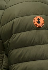 Veste matelassée vert olive avec un patch circulaire orange représentant un canard chanteur et le texte "SAVE THE DUCK" sur le haut de la poitrine.