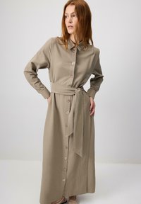 Long, khaki shirt dress with button front, collar, and belted waist. Textured fabric, long sleeves, and a straight cut to ankle length.