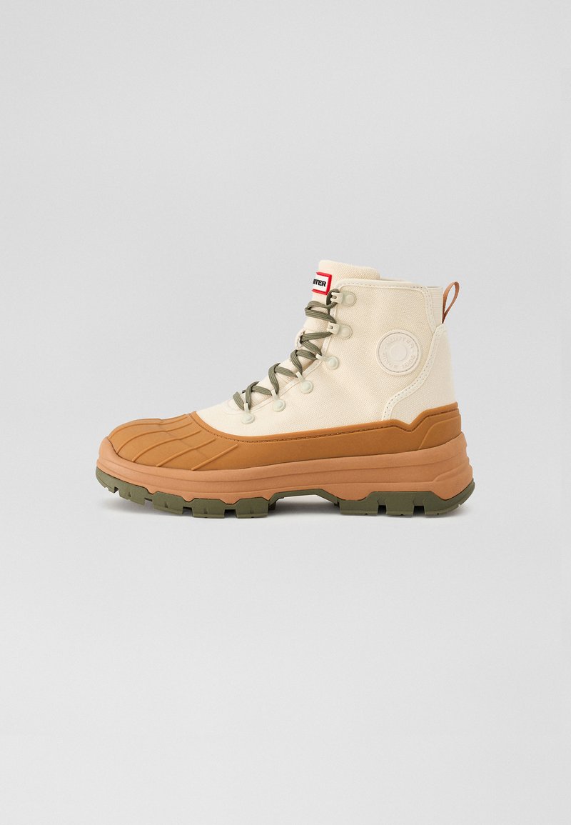 Beige high-top boot with a textured rubber sole, tan accents, green laces, and a logo patch, featuring a padded collar and an outdoor design.