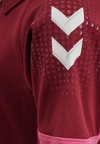 Marinröd sporttröja med en texturerad yta, rosa kant och vita chevron-accenter på axeln med prickdetaljer.