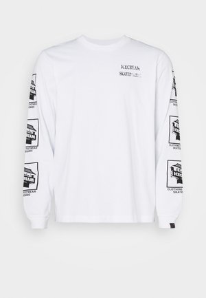 T-shirt blanc à manches longues en coton avec des graphismes imprimés noirs sur les deux manches et sur le devant, avec des détails de poignet côtelés.