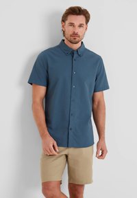 Short-sleeve, button-up shirt in solid dark blue cotton. Features a spread collar and front buttons, paired with beige shorts.
