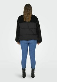 Czarna kurtka puchowa z puszystymi rękawami i pikowanym wzorem, zestawiona z niebieskimi dżinsami i czarnymi botkami za kostkę. Widok z tyłu ukazuje luźny krój.