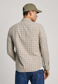 Camicia a maniche lunghe a quadri beige e blu con dettagli arancioni, in tessuto misto cotone, orlo curvo e polsini con bottoni, indossata con jeans blu.