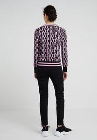 Suéter de punto en negro y rosa con un patrón de logotipos en toda la prenda, puños y dobladillo acanalados. Combinado con jeans ajustados negros y zapatillas negras.