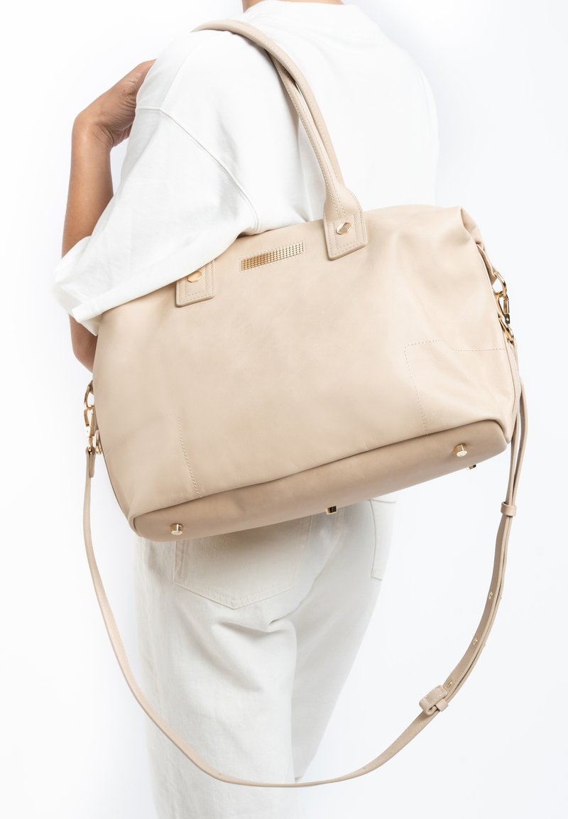 Beige leren handtas met dubbele handvatten en een afneembare schouderriem. Kenmerkt zich door goudkleurige hardware en een gestructureerd accent aan de voorkant.