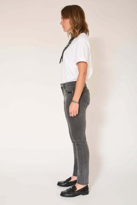 Jean skinny gris à texture lisse, associé à un t-shirt blanc et des mocassins noirs. La tenue comprend un détail de design subtil avec une écharpe.