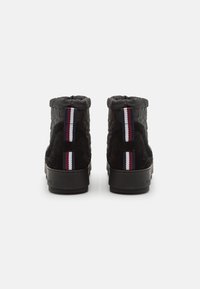 Sorte høje sneakers lavet af ruskind og tekstureret stof, med en tyk sål og en stribet detalje på bagsiden i marineblå, hvid og rød.