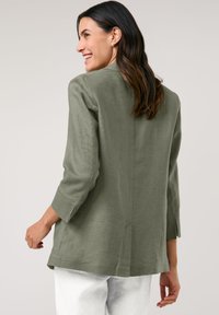 Olivengrüner, leichter Leinenblazer mit lockerer Passform, Dreiviertelärmeln, geschlitzen Rücken und einem einfachen, klaren Design.