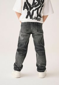 Mörkgrå denimjeans med avspänt snitt, med två bakfickor och lätt blekning. Kombination med vita sneakers och en kortärmad t-shirt med grafik.