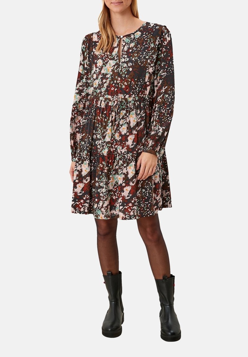 Robe à manches longues à motif floral avec une taille froncée, dans des tons foncés avec des accents roses et verts, associée à des bottines noires.