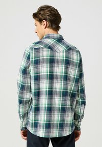 Męska koszula w kratę z zielonym, granatowym i białym schematem kolorów. Wykonana z miękkiego materiału, z długimi rękawami i zapinanymi mankietami. Klasyczny krój kołnierzyka.