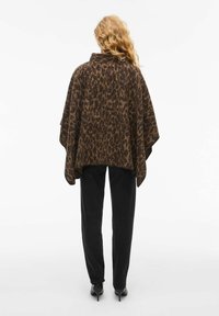 Tamsaus rudo ir tan leopardų rašto pončas, pagamintas iš minkštos medžiagos, su aukštu apykakle ir laisvais, plazdančiais rankovėmis; derinamas su juodomis kelnėmis.