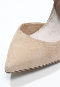 Chaussure pointue en daim beige avec empeigne basse et doublure claire visible à l'intérieur sur fond blanc.