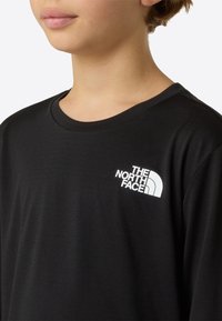 Tricou negru cu mâneci lungi din țesătură netedă, cu logo alb The North Face pe pieptul stâng. Design clasic cu guler rotund.