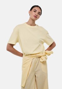 T-shirt en coton jaune à manches courtes et col rond, associé à un pantalon taille haute jaune et blanc à rayures cintré à la taille.